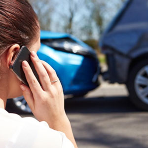 A woman inspecting a damaged car while on her phone for auto accident claims in Louisiana at Whitley-Sebti Law.